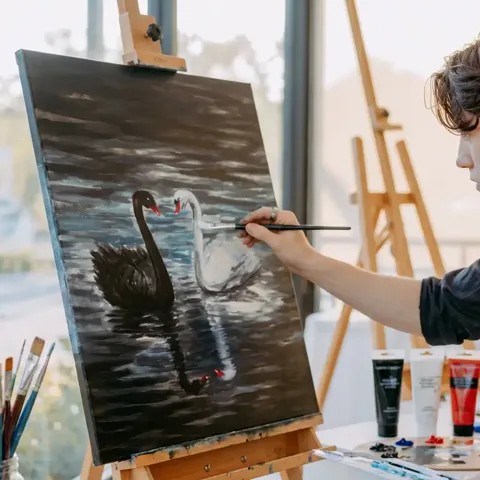 Module 5: the artist adding finishing touches to the completed black and white swan painting on the easel