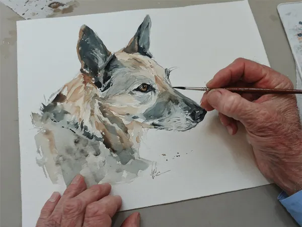 A hand rescuing a watercolor portrait of a German shepherd with a fine brush