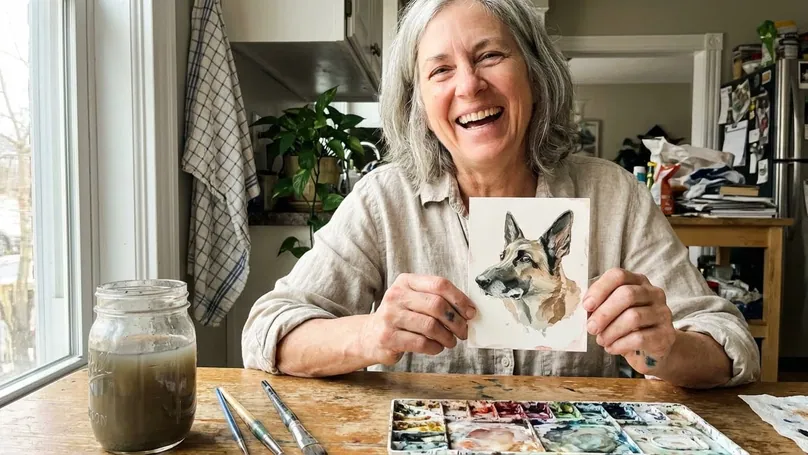 A delighted student in her kitchen holding up the realistic watercolor German shepherd portrait she just finished