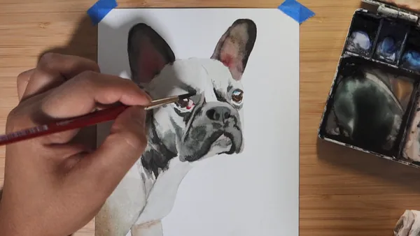 A brush adding detail to the eyes of a part-finished realistic watercolor dog portrait