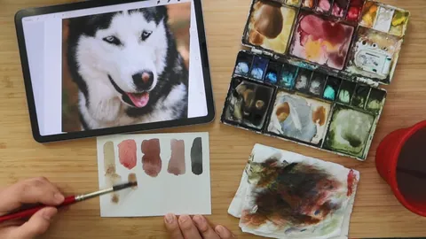 Mixing watercolor paints on a palette to match a dog's fur colour